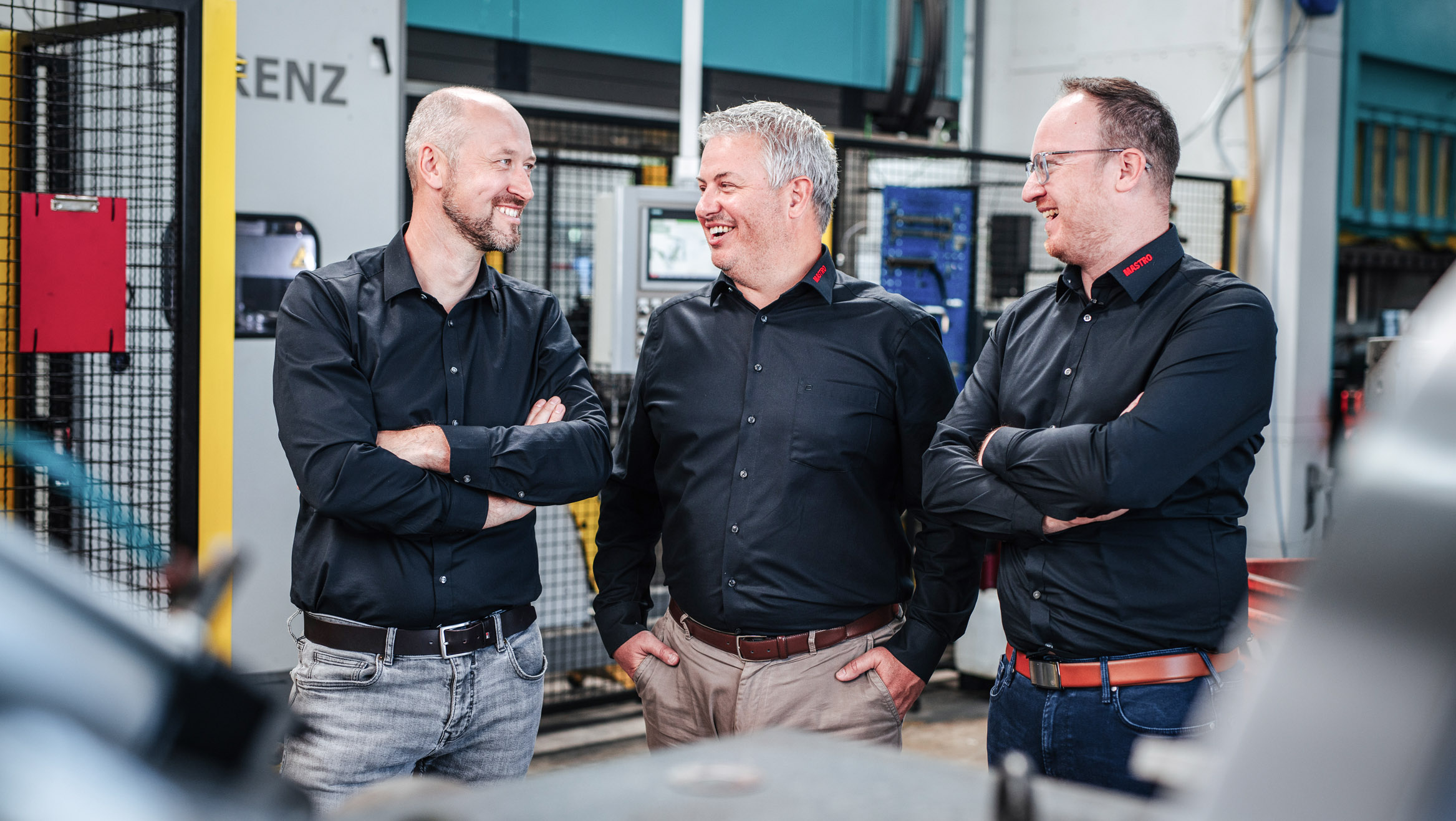 Die drei MASTRO-Geschäftsführer Florian Reiterer, Franz Müller und Werner Garber (von links nach rechts) stehen nebeneinander und plaudern in der Werkhalle.